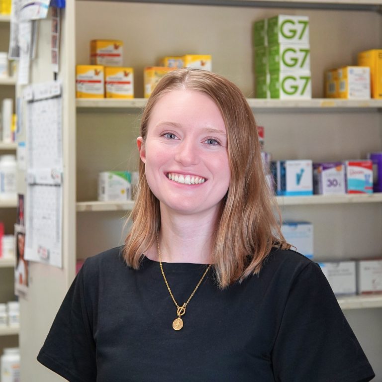 Portrait of a smiling woman in front of a pharmacy shelf with boxes of medication